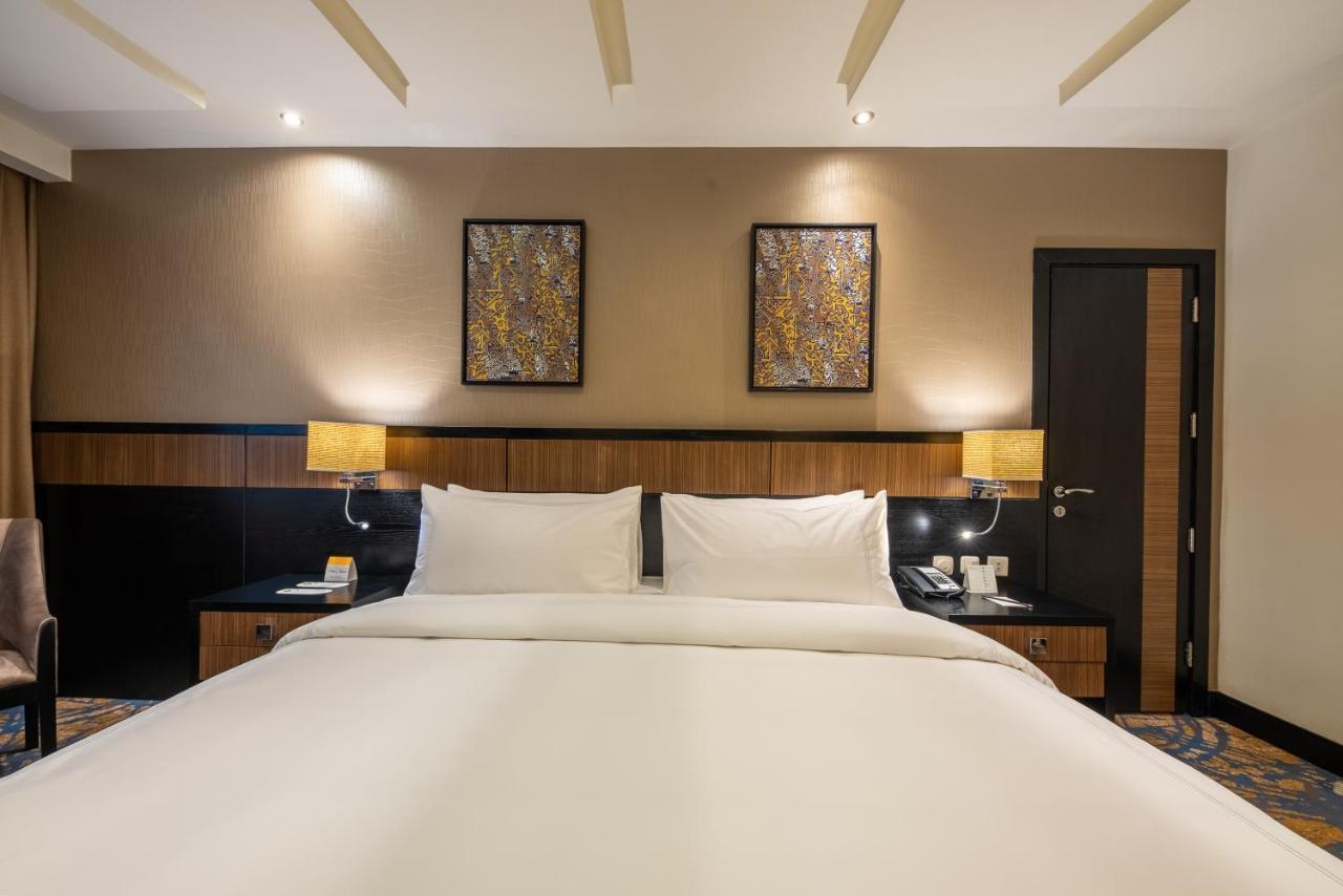 Al Ghufran Safwah Hotel Makkah Мекка Экстерьер фото The photo shows a hotel room featuring a large bed with white linens and two pillows. The background includes wooden elements, with bedside lamps on either side of the bed. Above the bed, there are two decorative wall art pieces. A dark-colored door 