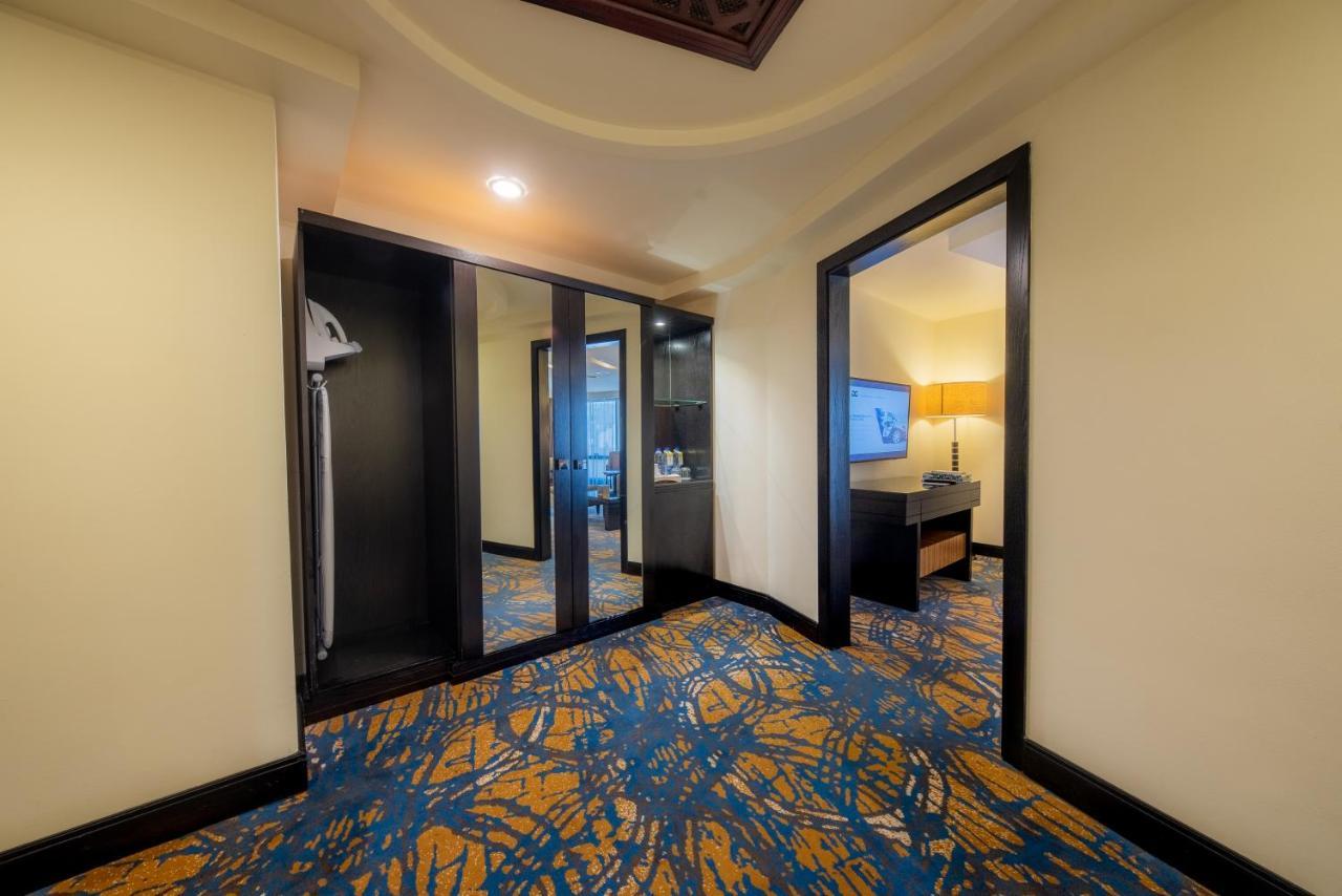Al Ghufran Safwah Hotel Makkah Мекка Экстерьер фото The photo shows the interior of a hotel room. There is a small entryway with a patterned carpet featuring blue and yellow colors. On one side, there is a closet with mirrored doors. Opening into the room, there are two doorways: one leads to a bathro