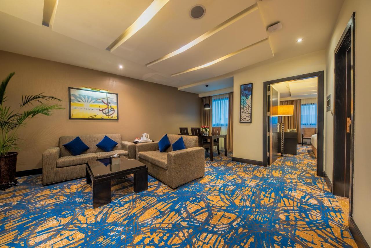 Al Ghufran Safwah Hotel Makkah Мекка Экстерьер фото The photo shows a modern and well-decorated living area, likely in a hotel suite or a well-appointed home. 

- **Furniture**: There are two light-colored sofas with blue cushions, arranged around a dark coffee table. 
- **Artwork**: On the wall, ther