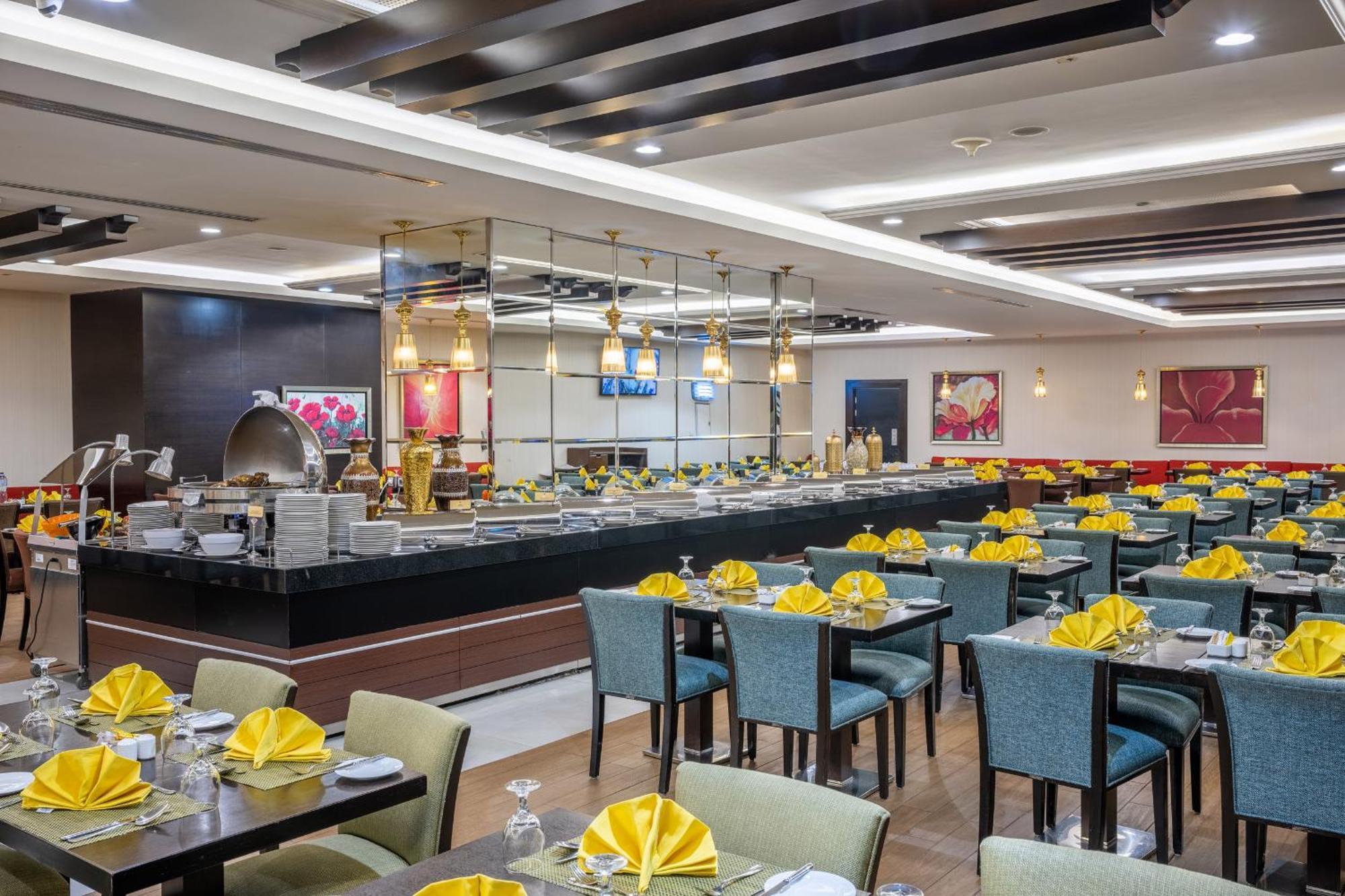 Al Ghufran Safwah Hotel Makkah Мекка Экстерьер фото The photo shows a spacious restaurant interior. There are neatly arranged tables with blue chairs, each set with yellow napkins and silverware. In the background, there's a buffet area with an open layout featuring various food displays. The decor ap