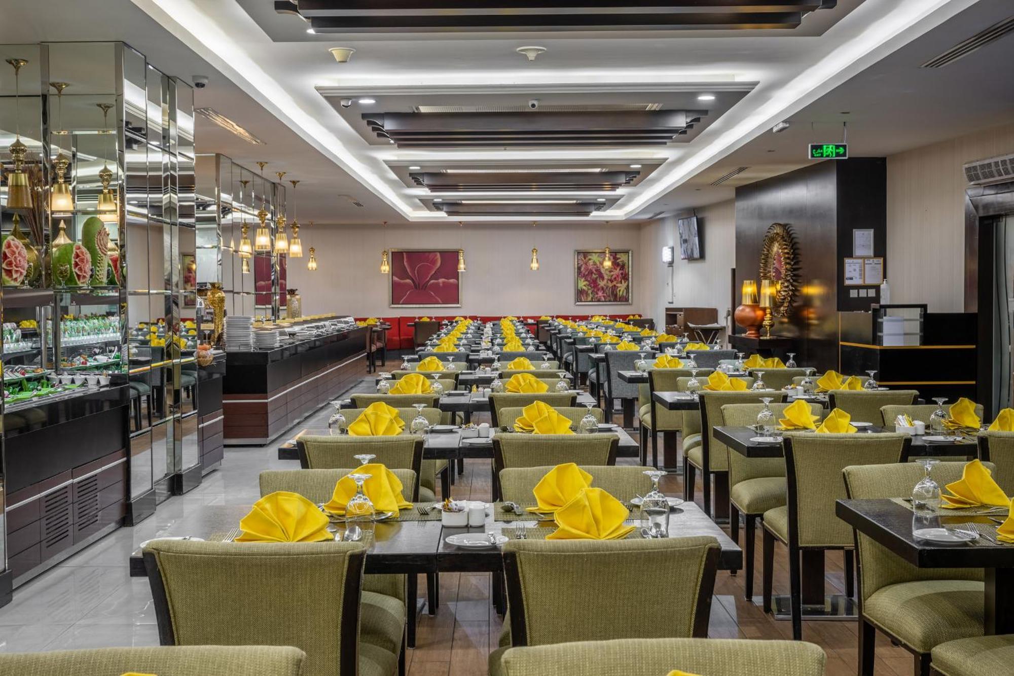 Al Ghufran Safwah Hotel Makkah Мекка Экстерьер фото The photo shows the interior of a restaurant. The dining area features multiple rows of tables, each set with yellow napkins and glassware. The tables are covered with dark-colored tablecloths and are surrounded by green upholstered chairs. The resta